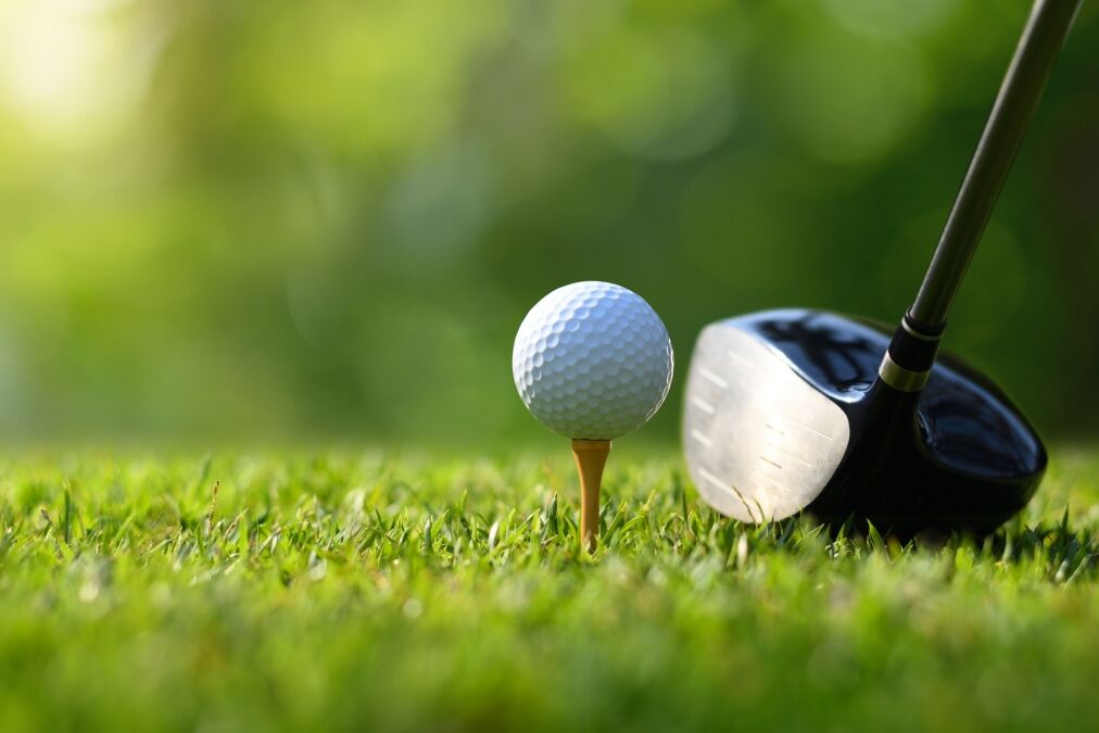 Close-up golf ball on tee with golf drivers at golf course.