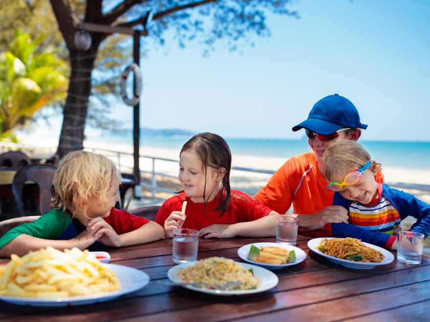 Family eating lunch on tropical beach. Kids in outdoor restaurant of exotic resort in Asia. Asian food for children. Young man, boy and girl eat dinner at sea coast. Holiday with child.