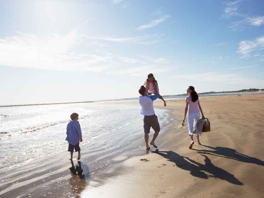 Rear View Of Family Walking Along Beach With Picnic Basket