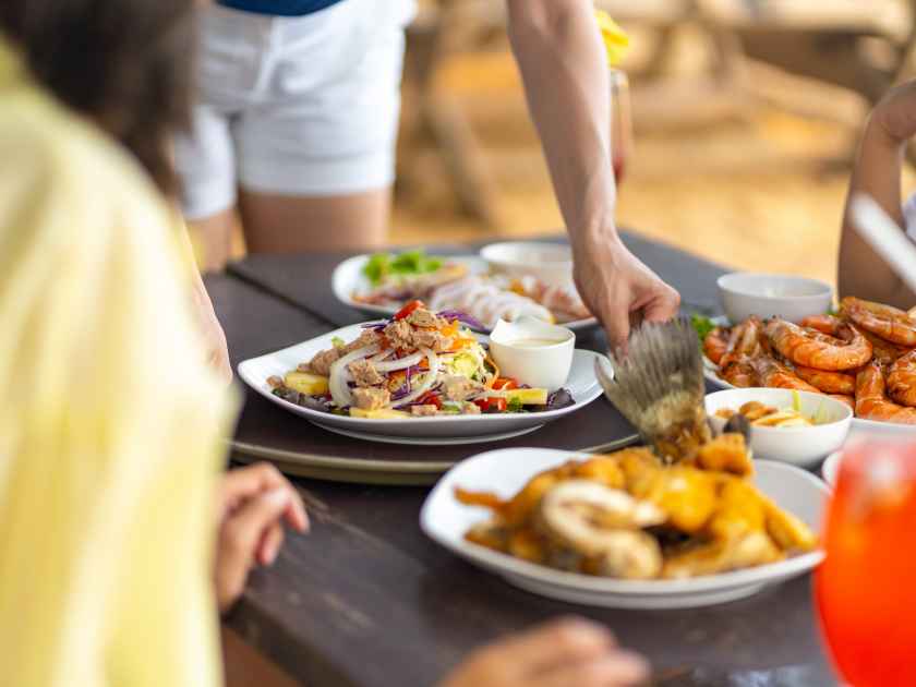 Happy Asian family couple and little kids travel ocean on summer holiday vacation. Waitress serving food and drink to customers on the table at beach restaurant at tropical island beach in sunny day.