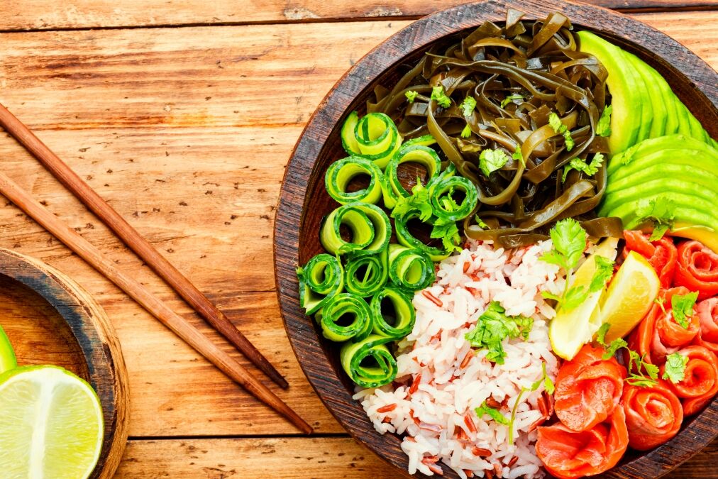 Poke bowl with salmon and vegetables on wooden table