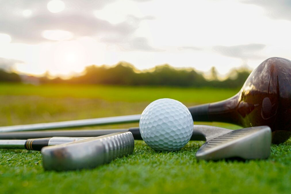 Close up old golf club and golf ball on green grass with sunset background. Golf ball and wooden driver on green grass background.