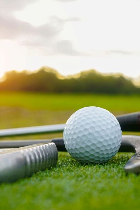 Close up old golf club and golf ball on green grass with sunset background. Golf ball and wooden driver on green grass background.