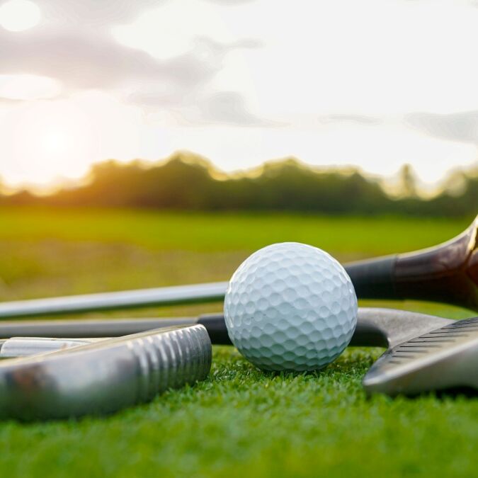 Close up old golf club and golf ball on green grass with sunset background. Golf ball and wooden driver on green grass background.