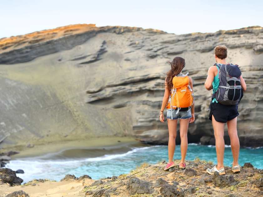 Hikers - travel couple tourists hiking on Hawaii. Tourist backpackers walking on Green Sand Beach, Papakolea on Big Island, Hawaii, USA. Young happy couple traveling with backpacks.