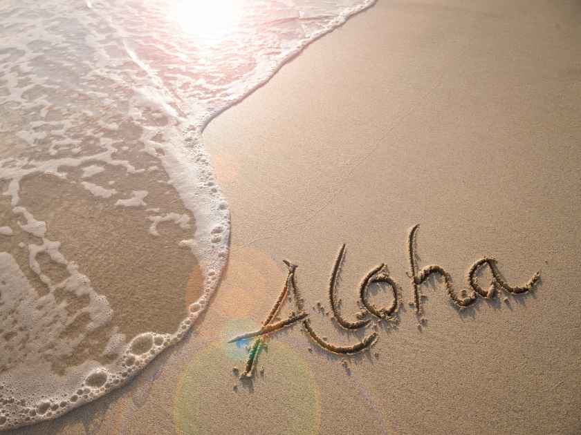 Aloha tropical vacation message handwritten on a smooth sand beach with incoming wave