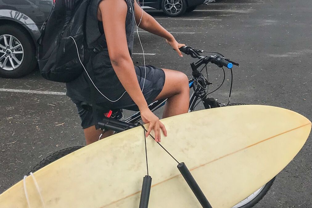 A surfboard on carrier. Man carries a surfboard riding a bicycle on the road parking lot at Lahaina city. A young Asian man smiling , Maui, Hawaii, U.S.A the popular surf city