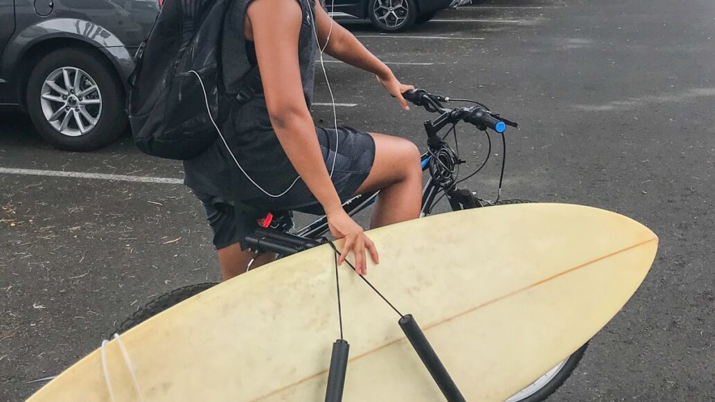 A surfboard on carrier. Man carries a surfboard riding a bicycle on the road parking lot at Lahaina city. A young Asian man smiling , Maui, Hawaii, U.S.A the popular surf city