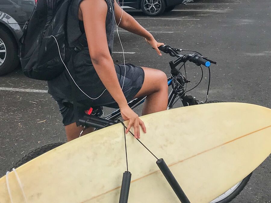 A surfboard on carrier. Man carries a surfboard riding a bicycle on the road parking lot at Lahaina city. A young Asian man smiling , Maui, Hawaii, U.S.A the popular surf city