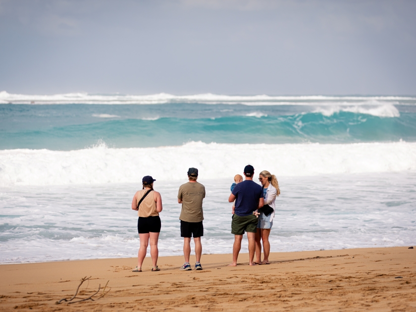 Kapa'a, Hawaii US - February 17, 2024: a group of 4 adults with a baby watching high surf at Ha'ena Beach Park on the North Shore of Kauai, Hawaii. Tourists at Haena Beach.