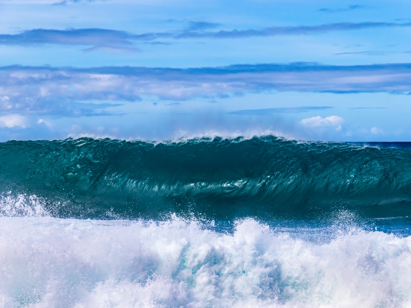 Wave breaking on the western Kona coast of Hawaii's Big Island. Spray and foam in foreground. Pacific ocean, sky with clouds beyond.