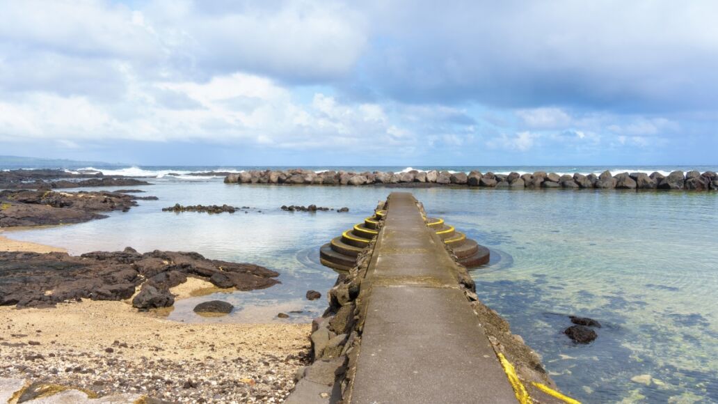 Beautiful Hawaii beach with a sandy shoal and a stone pier with steps for easy access to the water, separated from the ocean by a massive stone barrier.