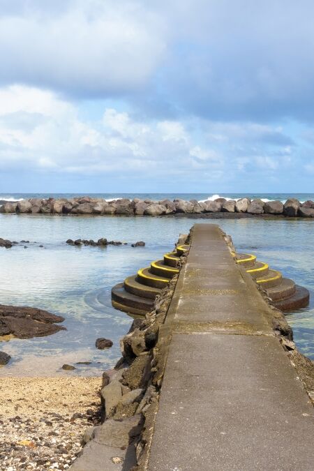 Beautiful Hawaii beach with a sandy shoal and a stone pier with steps for easy access to the water, separated from the ocean by a massive stone barrier.