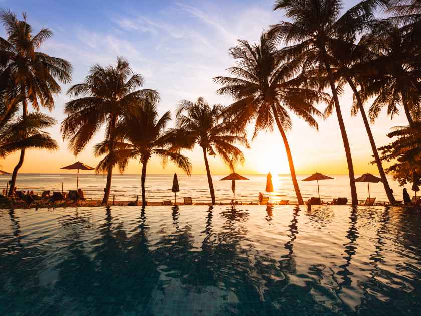 beautiful sunset on the beach, holidays background, reflection of silhouettes of palm trees in swimming pool of hotel