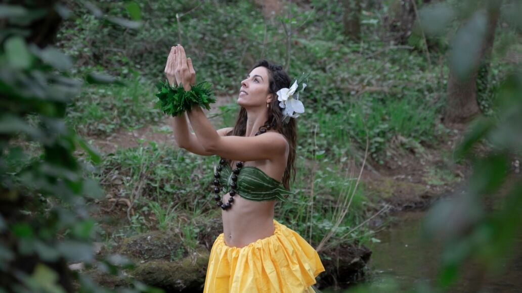 A young woman is looking at the sky with her hands together performing a typical Hawaiian dance connecting with nature.