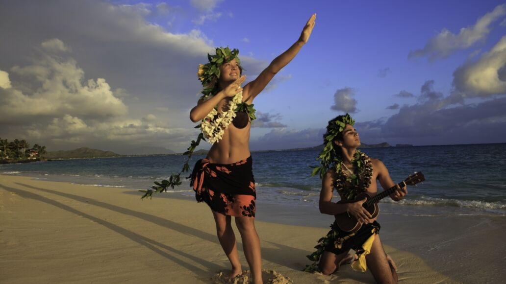 couple dancing hula on the beach at sunrise with the man playing ukulele