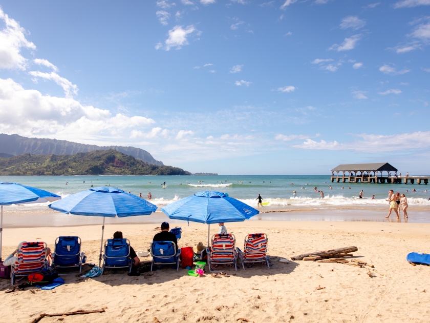 Hanalei, Hawaii US - February 22, 2024: tourists at Hanalei Bay Beach, north shore of Kauai, Hawaii. Sandy Hawaiian beach full of people sunbathing and playing in the ocean, on sunny day, Napali Coast