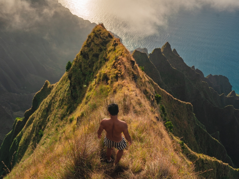 A man watching Sunset on Kalepa ridge Trail, Kalalau lookout. Hawaii, Kauai. Close to the edge.