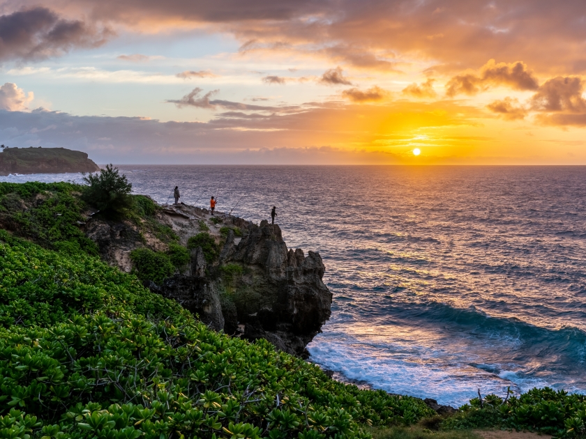 Men, fishermen, standing, fishing, on the edge of a cliff over the ocean, with the sun rising over the horizon and a partly cloudy sky, Mahaulepu Heritage Trail, Kauai, Hawaii