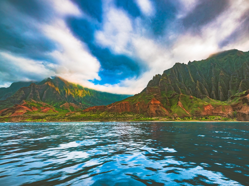 A boat tour view of Kalalau beach and Kalalau Valley during the sunset hour in the colorful and dramatic Nā Pali Coast State Wilderness Park on the island of Kauai, Hawaii, United States.