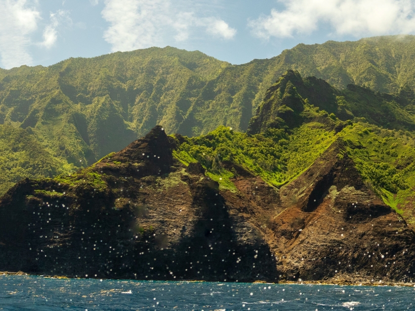 A panoramic view of the Na Pali Coast in Kauai, Hawaii, with lush green mountains and clear blue ocean