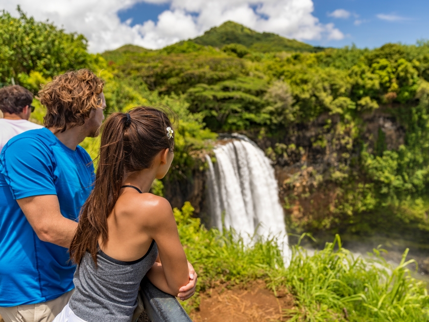 Couple tourists at Hawaii Kauai waterfall. Tourist visiting the Wailua Falls of Kauai Hawaii, hiking nature mountain vacation USA travel.