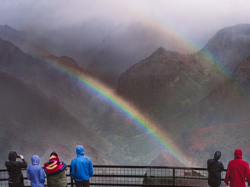 People looking at Waimea Canyon on Kauai island, Hawaii, on rainy and foggy day; double rainbow over the canyon