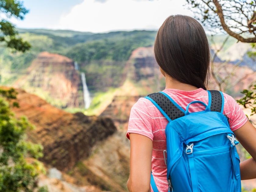 Hawaii hiking girl looking at Kauai waterfall. Woman hiker at Waipoo falls, Waimea Canyon, Hawaii. Kauai travel. Backpacker on hike trail in hawaiian forest overlooking mountains. Nature wanderlust.