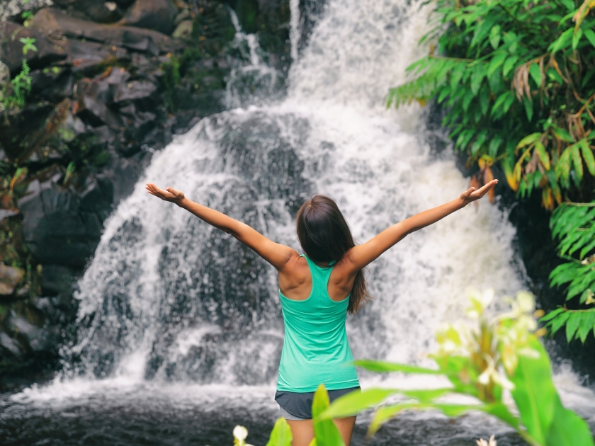 Hawaii travel nature waterfall woman hiker at Canyon Trail Waipoo Falls in Waimea, Kauai island, USA. Freedom happy girl with open arms meditating yoga in rainforest.