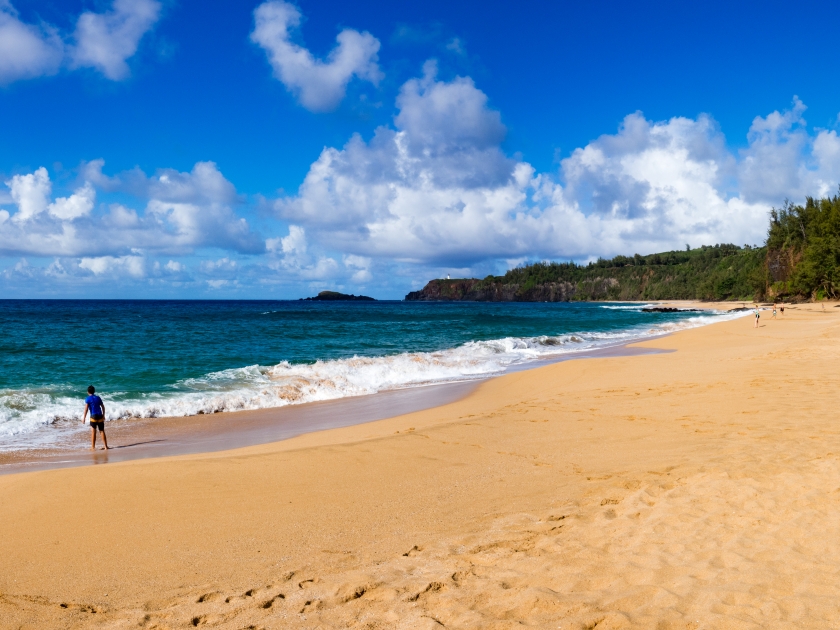 Boy playing at Secret Beach (Kauapea), Kauai, Hawaii, USA, summer day, sunny, Kilauea ilighthouse n distance