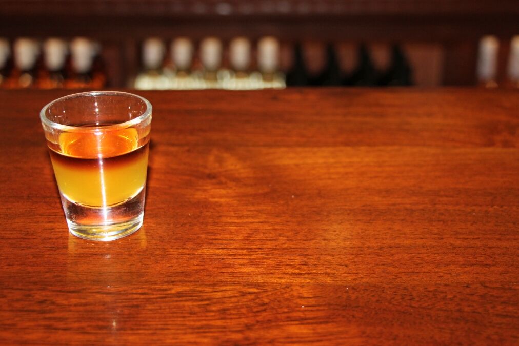 Koloa Rum on Kauaii, Hawaii - detail on the shot with dark coffee rum on the wooden table with blurred bottles in the background.