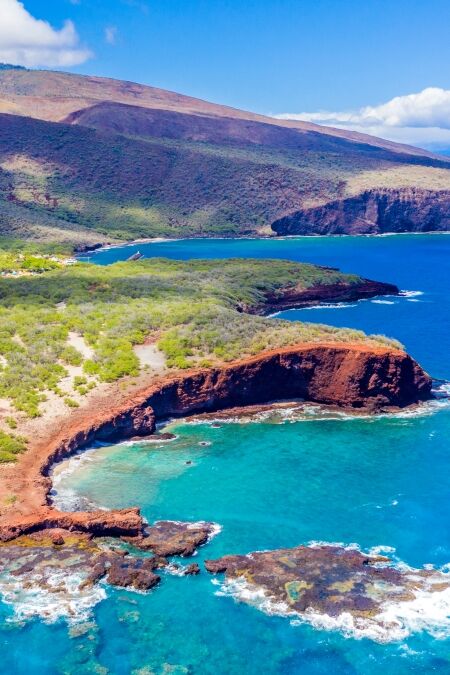 Aerial view of Lanai, Hawaii featuring Hulopo'e Bay and beach, Sweetheart Rock (Pu'u Pehe), Shark's Bay, and the mountains of Maui in the background.