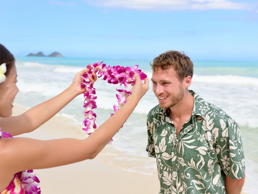 Hawaii woman giving lei garland of pink orchids welcoming tourist on Hawaiian beach. Portrait of a Polynesian culture tradition of giving a flower necklace to a guest as a welcome gesture.