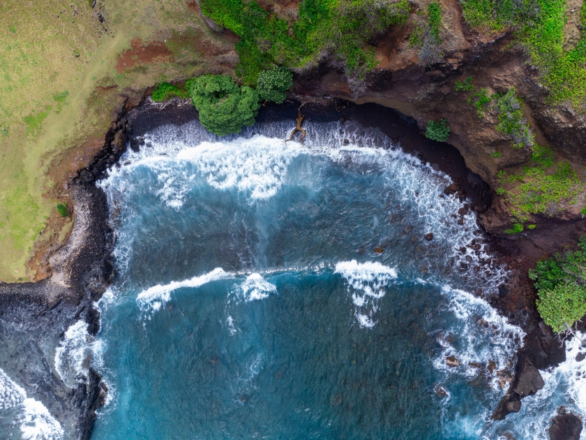 Hawaiian Black Sand Beach. A top-down aerial photo of waves crashing onto a black sand beach in Maui, Hawaii