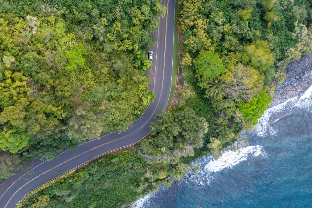 An aerial view of a winding road along a lush tropical coastline with crystal clear turquoise water. Road to Hana, Maui Hawaii.