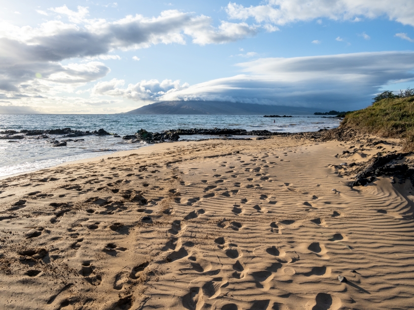 Many footprints in golden sand on the beach leading around the coastline at sunset, Kamaole Beach Park III, Maui, Hawaii