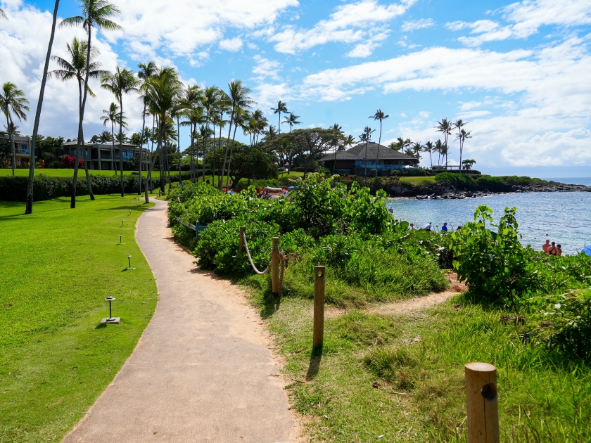 Walking path on the Kapalua Coastal Trail winding between luxury apartment buildings and the beach on Kapalua Bay in West Maui, Hawaii