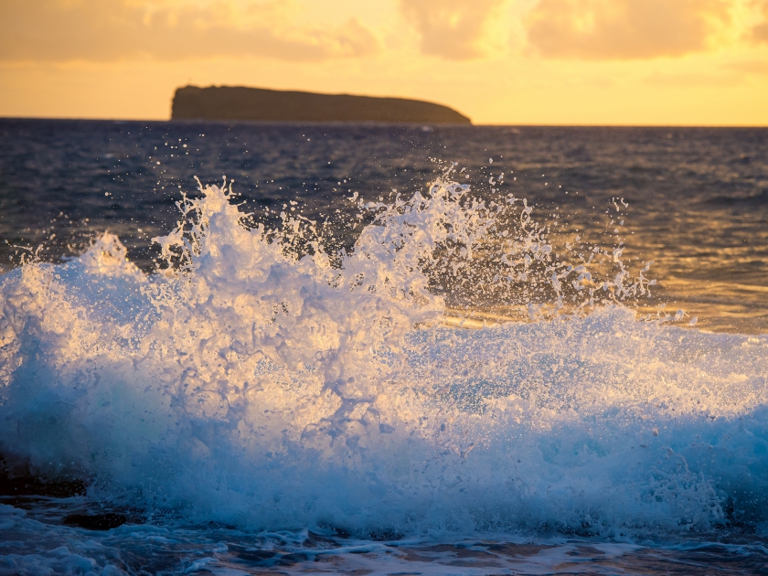 Molikini crater seen from Maui as waves crash on the rocks of Makena beach.