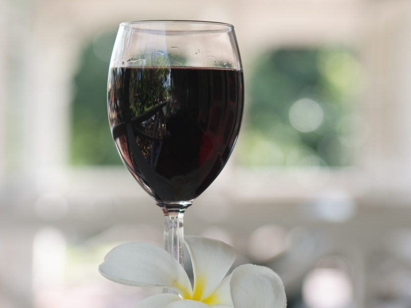 A glass of red wine and two plumeria blossoms on a balcony