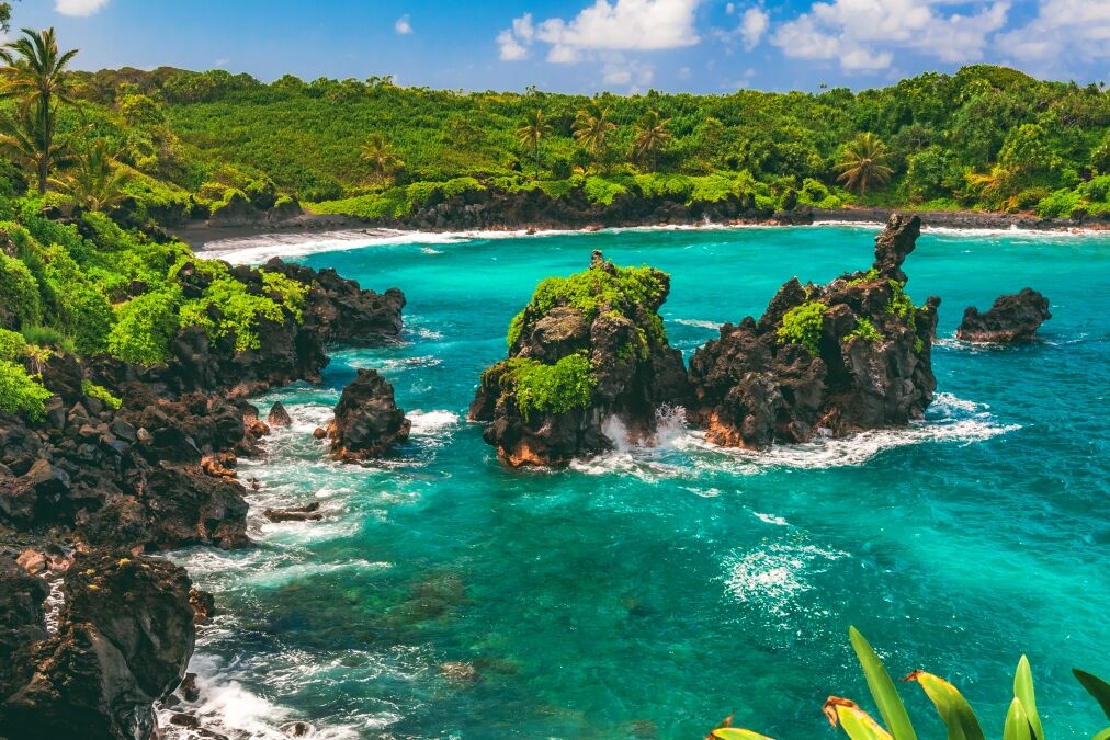 Black lava rock sea stacks sit in turquoise water just beyond the black sand beach of Waiʻanapanapa State Park in Hana on the island of Maui, Hawaii, United States.