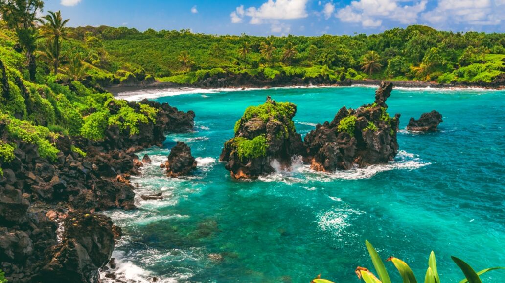 Black lava rock sea stacks sit in turquoise water just beyond the black sand beach of Waiʻanapanapa State Park in Hana on the island of Maui, Hawaii, United States.