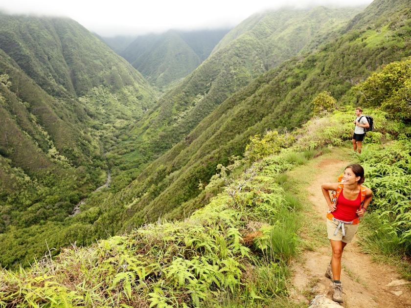 Hiking people on Hawaii, Waihee ridge trail, Maui, USA. Young woman and man hikers walking in beautiful lush Hawaiian forest nature landscape in mountains. Asian woman hiker in foreground.