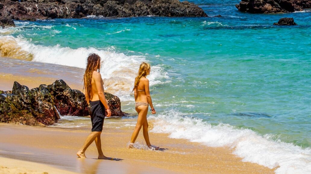 A couple enters the warm waters of the Pacific Ocean at Waimea Bay on the north shore of Oahu, Hawaii.