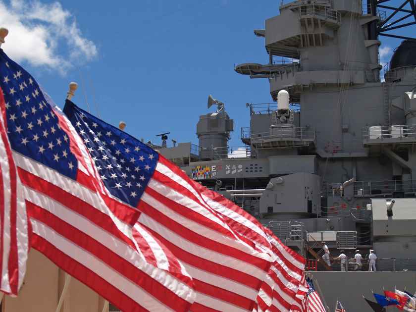 US flags flying beside the Battleship Missouri in Pearl Harbor, Honolulu, Oahu, Hawaii with 4 sailors walking on deck.