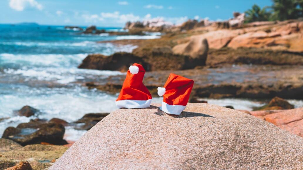 Couple of santa claus hat on tropical exotic paradise sandy beach with ocean waves and rocky coastline in background