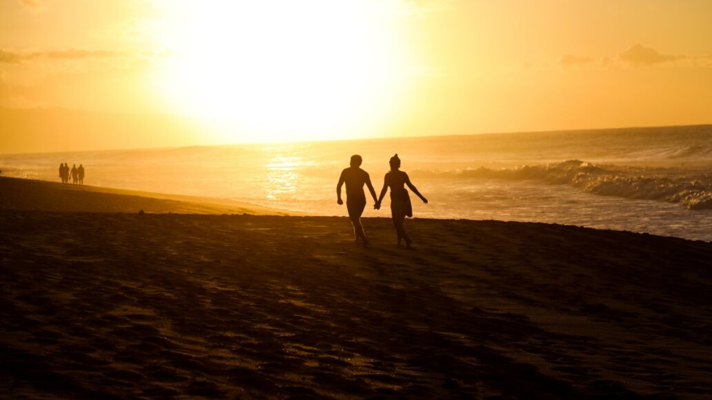 Romantic Couple Holds Hands While Walking on Beach in Oahu Hawaii near Banzai Pipeline at Sunset