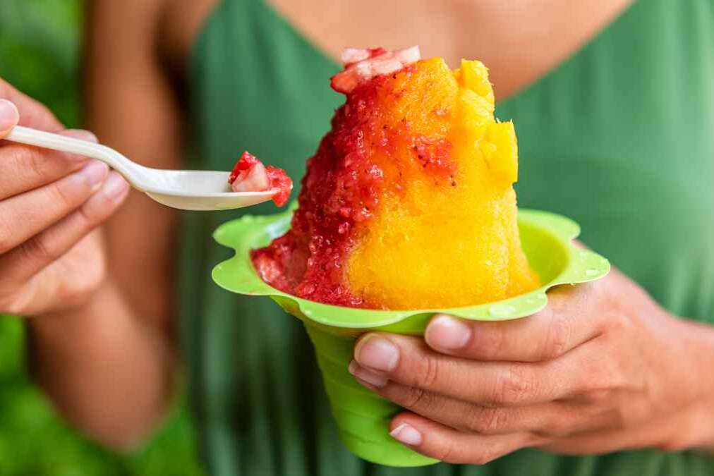 Shave Ice Hawaii local food woman eating hawaiian shaved ice cream treat in Honolulu Waikiki beach, Hawaii , USA.