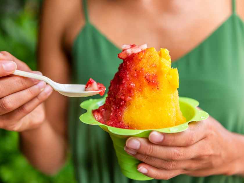 Shave Ice Hawaii local food woman eating hawaiian shaved ice cream treat in Honolulu Waikiki beach, Hawaii , USA.