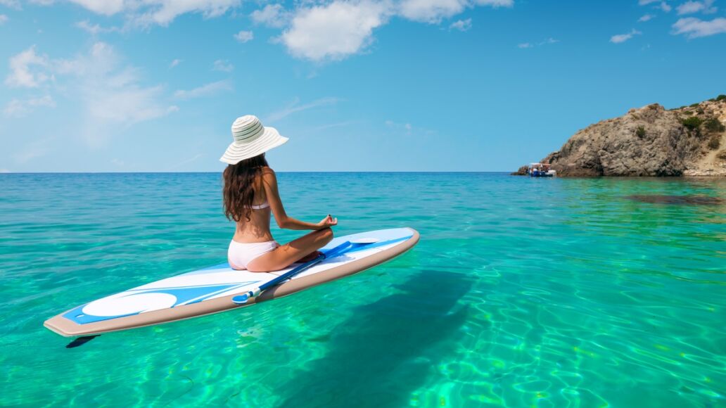 A beautiful young woman relaxes on a SUP board in the sea near the island. Standup paddleboarding on Hawaii.