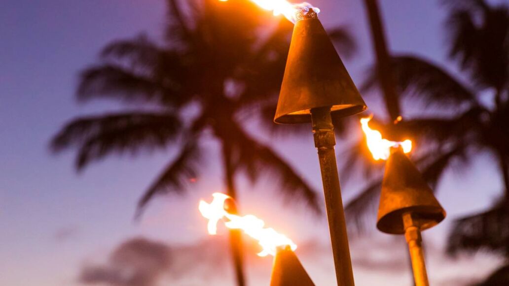 Hawaii sunset with lit tiki torches. Hawaiian icon, lights burning at dusk at beach resort or restaurants for outdoor lighting and decoration, cozy atmosphere.